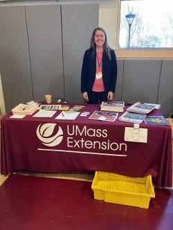 Maria Gannett standing behind a table with a UMass Extension tablecloth with many pamphlets and handouts displayed.