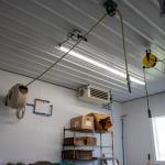 A hose reel attached to a wall, with a hose coming out of it then running through a hose guide attached to the ceiling further along, then dropping to the floor.