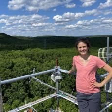 Ashley Keiser stands on a platform overlooking the mountains on a beautiful partly cloudy day