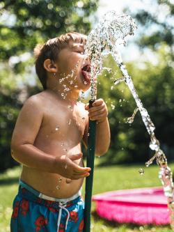 Young boy drinking from a garden hose