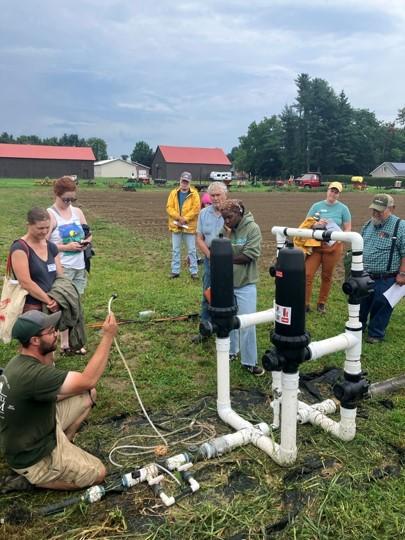 A group of people gathered around someone showing an irrigation setup.