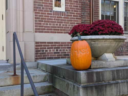 A pumpkin on the steps of a building. The pumpkin has "UMass" etched into the skin.